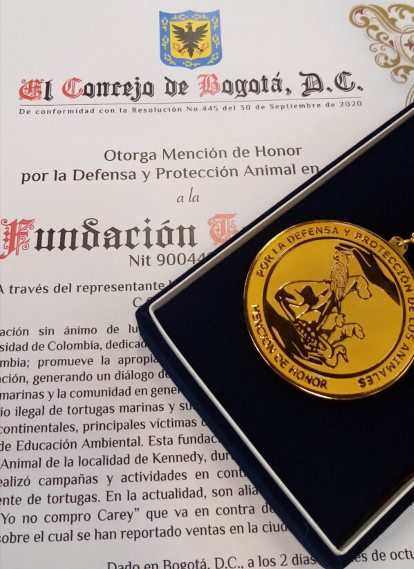 Foto de la mención de honor y medalla otortgada por el concejo de Bogotá. La medalla es dorada con un diseño en el centro de varios animales en medio de dos manos, una arriba y otra abajo. La cinta de la medalla es amarilla y roja, como los colores de la bandera de Bogotá.