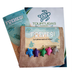 Fotografía del juego "Frenesí: La carrera hacia el océano". En el centro destaca una bolsa de yute que contiene cinco fichas de plástico con forma de tortuga marina en colores azul, morado, verde, rosa y gris. La bolsa tiene una etiqueta con el nombre del juego, ilustraciones de tortugas y una advertencia para mayores de 7 años. Al fondo, se observa el folleto de instrucciones azul y una tarjeta blanca con el logotipo de la "Fundación Tourtugas".